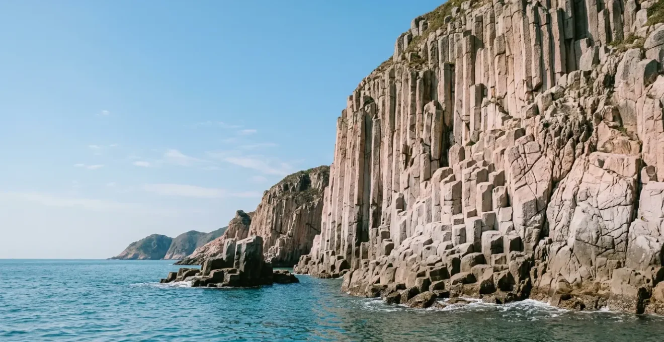 Dramatic coastal view of towering hexagonal volcanic rock columns rising from turquoise waters in Hong Kong UNESCO Global Geopark