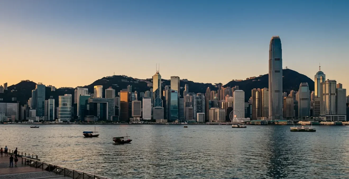 Hong Kong skyline featuring iconic skyscrapers along Victoria Harbour with mountain backdrop at golden hour