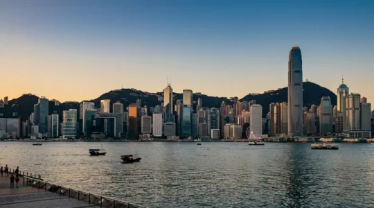 Hong Kong skyline featuring iconic skyscrapers along Victoria Harbour with mountain backdrop at golden hour
