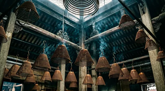 Hanging spiral incense coils glowing in dim temple light with atmospheric smoke rising upward