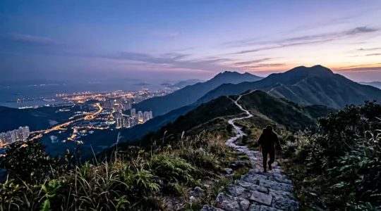 Hiker ascending stone steps toward Lantau Peak summit at pre-dawn hour with city lights visible below