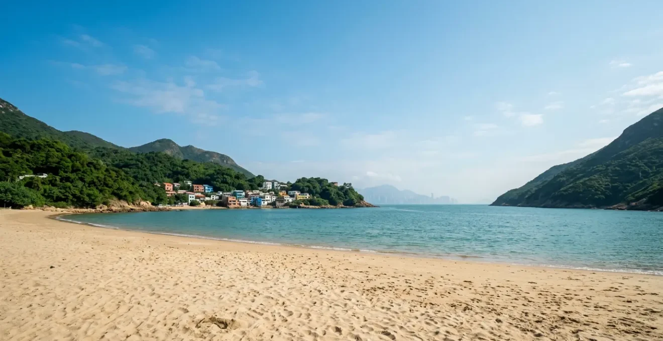 Wide-angle view of Shek O Beach with golden sand, turquoise waters, and green mountains under blue sky