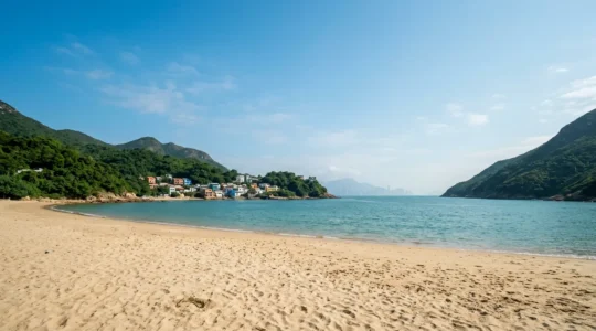 Wide-angle view of Shek O Beach with golden sand, turquoise waters, and green mountains under blue sky
