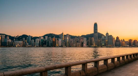 Golden hour view of Victoria Harbour from Tsim Sha Tsui waterfront with Hong Kong Island skyline reflecting on calm waters