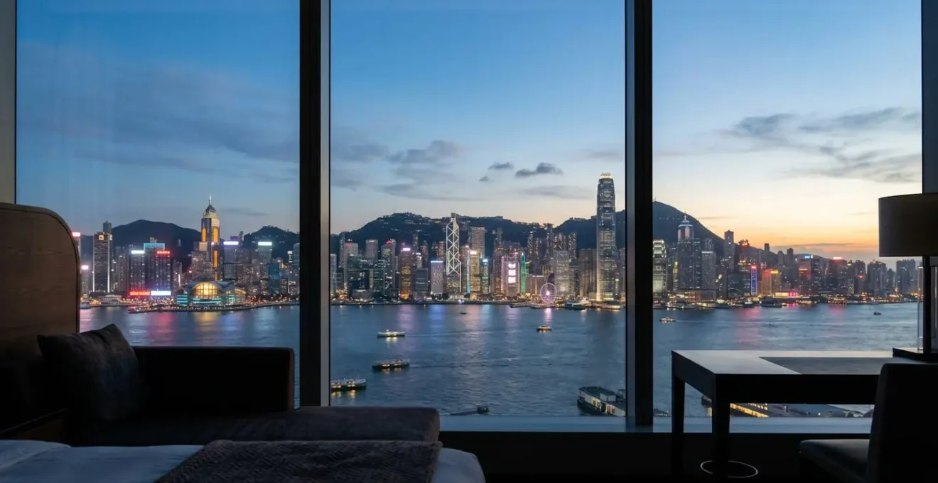 Panoramic harbor view from luxury hotel window at twilight with illuminated Hong Kong skyline