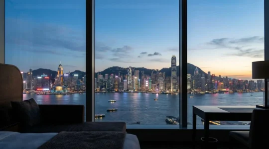 Panoramic harbor view from luxury hotel window at twilight with illuminated Hong Kong skyline
