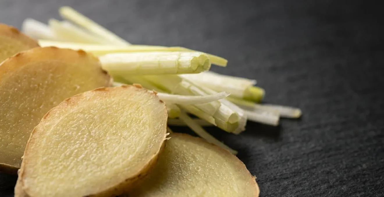 Macro shot of fresh ginger slices and spring onion on a cutting board, highlighting the subtle aromatics used in Cantonese cooking