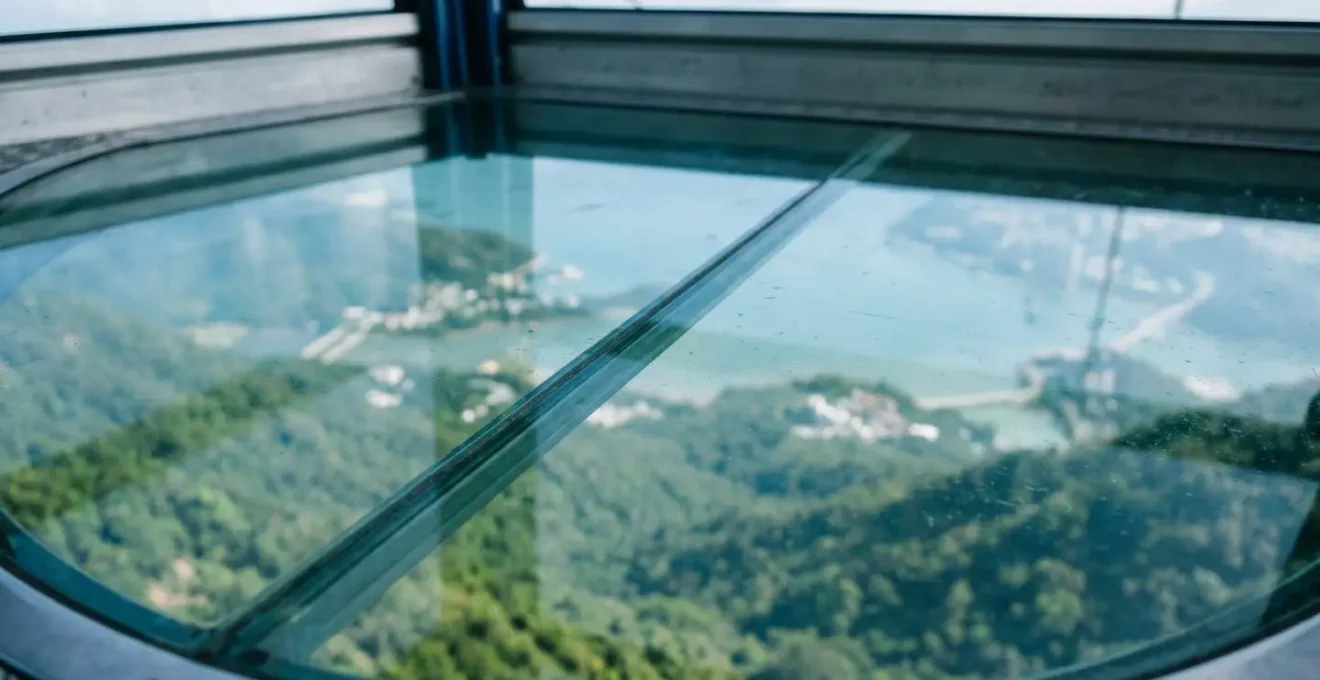 Close-up view through transparent glass floor of cable car cabin showing mountainous Lantau terrain and turquoise waters below