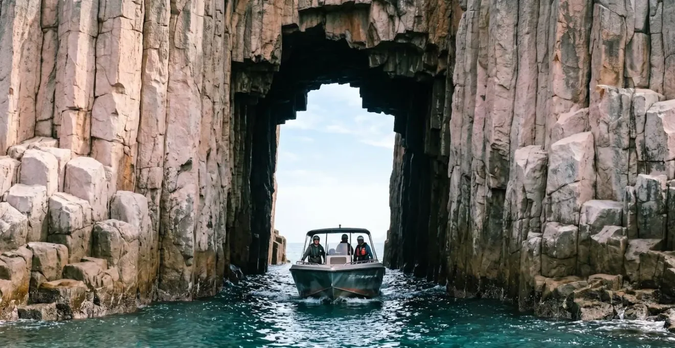 Speedboat navigating through a dramatic hexagonal rock column sea arch in Hong Kong Geopark waters