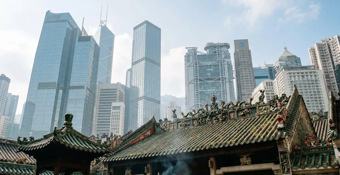 Ancient Chinese temple rooftop with green glazed tiles framed against Hong Kong modern glass skyscrapers in atmospheric misty morning light