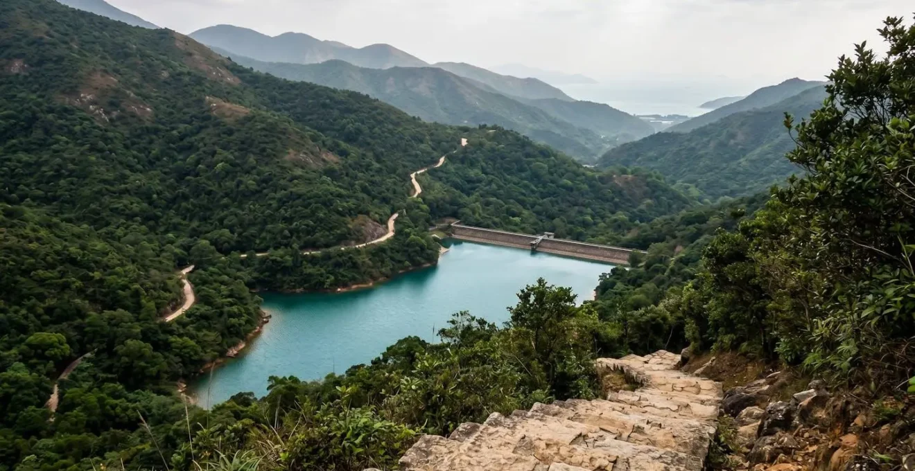 Turquoise reservoir waters surrounded by steep forested slopes with winding mountain trail visible