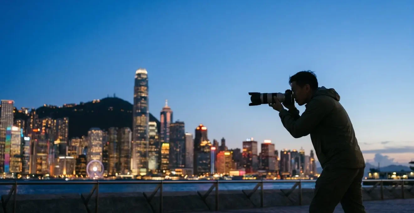 Photographer silhouette holding telephoto lens aimed across Victoria Harbour toward compressed urban skyline at dusk